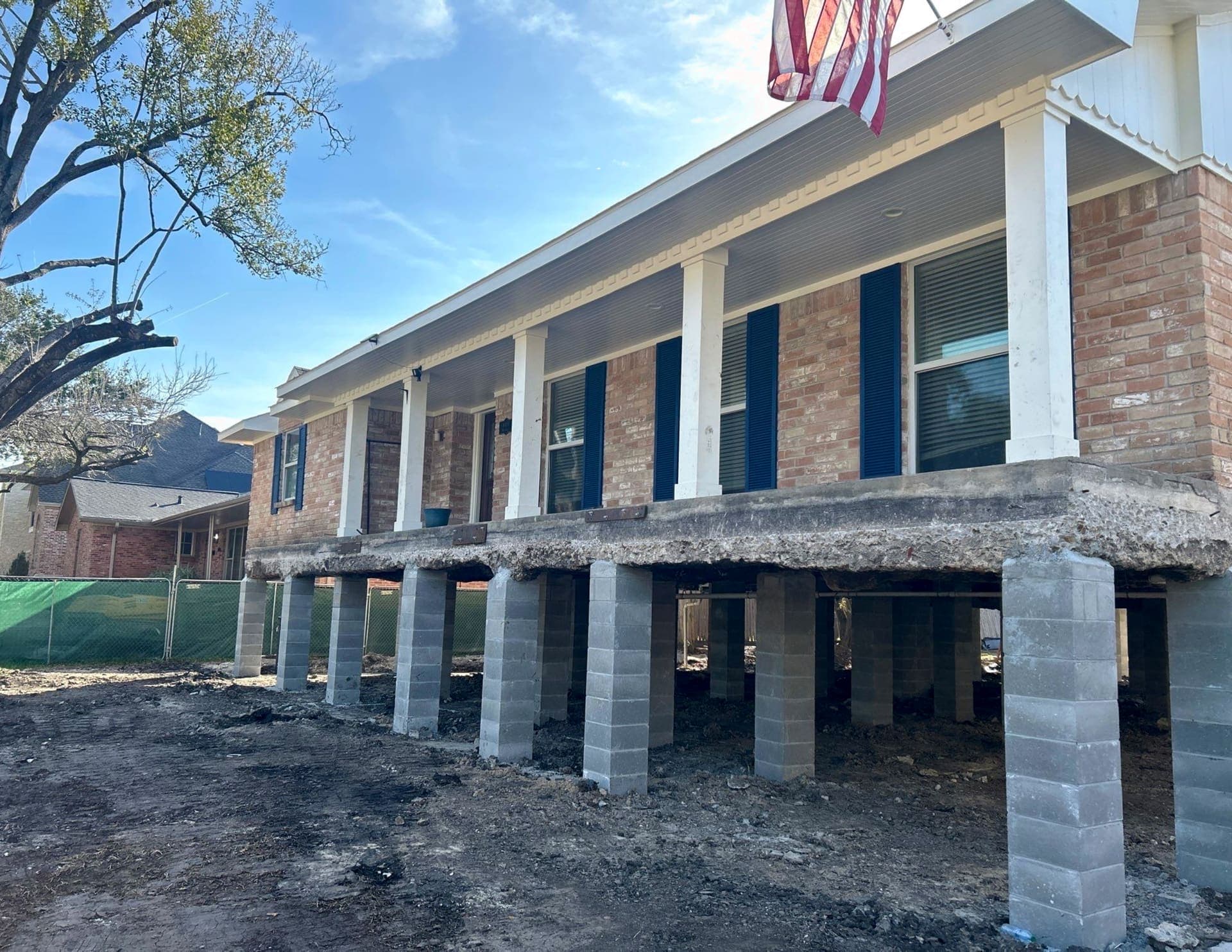 Raised home with black shutters, white columns, and an American flag after elevation onto columns